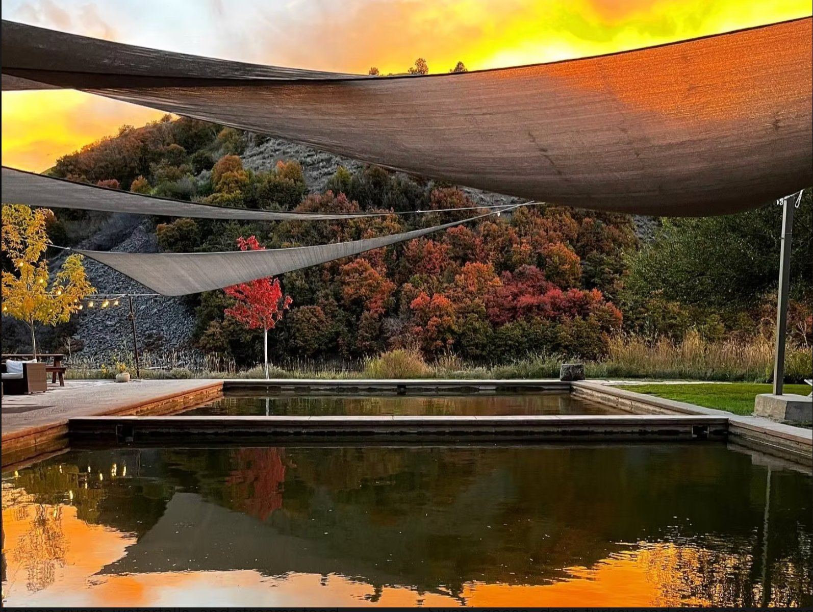Shade sails over the mineral soaking pool at sunset, autumn hillside behind